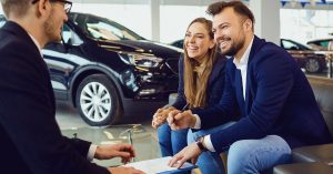 Couple signing documents with a car dealer in showroom for an Income-Based Car Lease approval