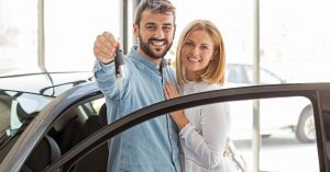 First-Time Car Buyers receiving car keys from a dealership while standing beside their newly purchased vehicle.